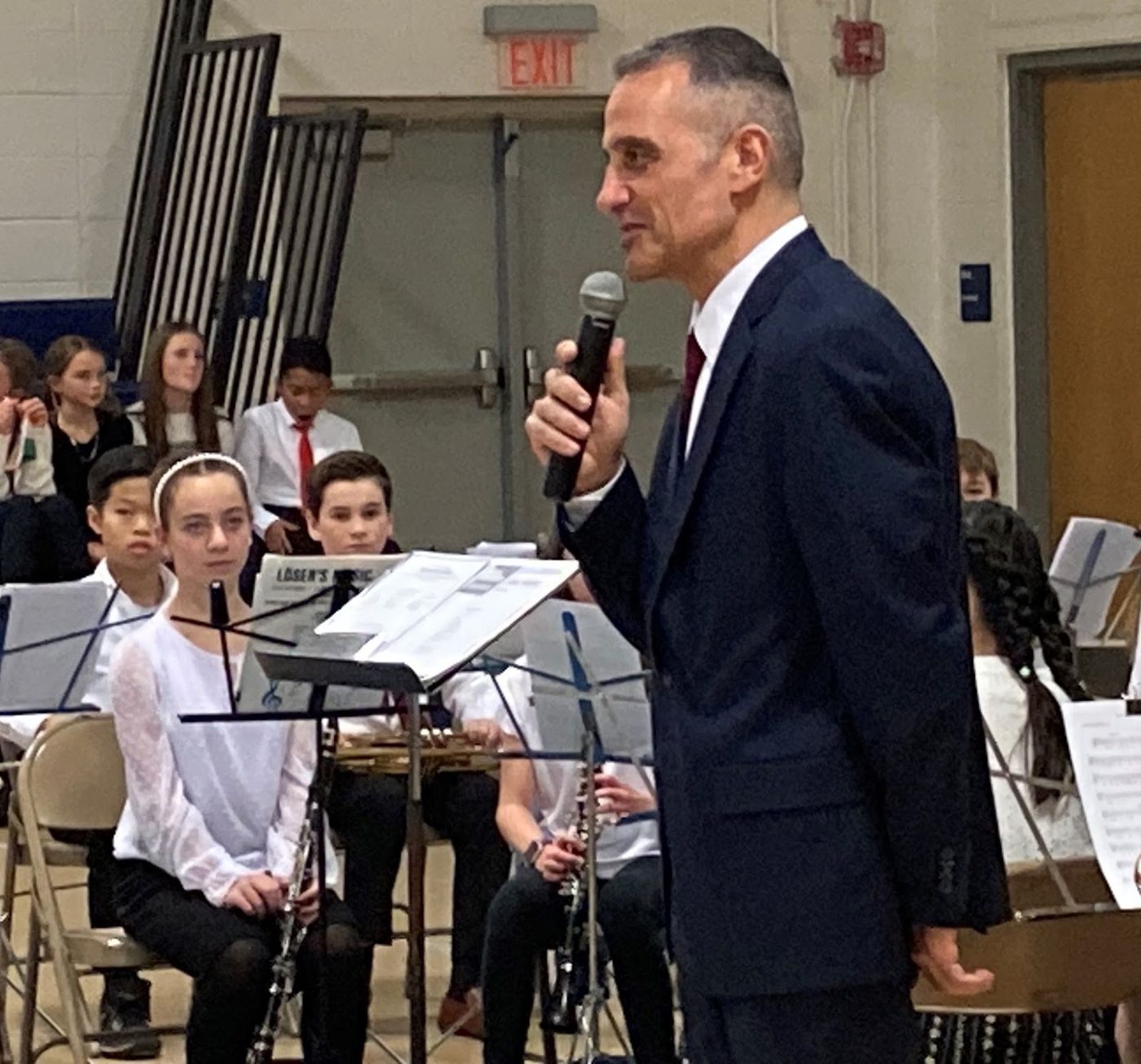 Mr. Papazian speaking to the audience at a concert, students seated with their instruments behind him